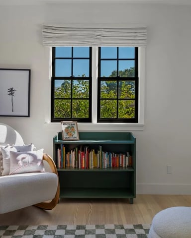 Bright children's room with a rocking chair, green bookshelf, and garden-view windows